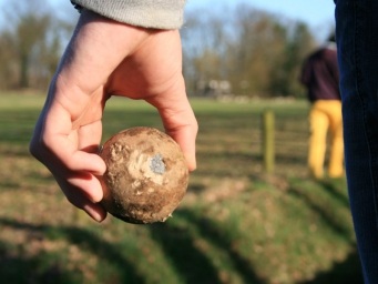 Klootschieten in de Donkere Duinen naast klimbos De Klimvallei: Hand met klootschietbal in focus, terwijl op de achtergrond een groep bezig is met klootschieten.