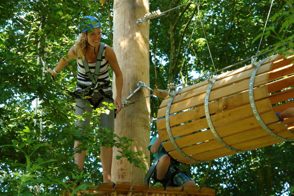 Avontuurlijke vrouw beklimt met succes een hindernis in De Klimvallei te Den Helder, klaar voor de volgende uitdaging met de tonnen.